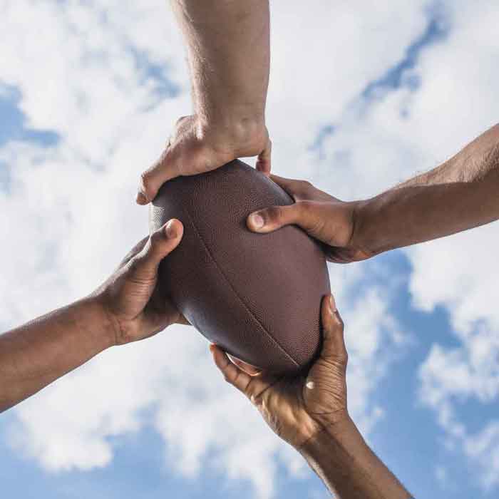 Hands holding football with blue sky in background.